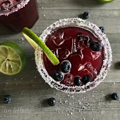 two glasses filled with blueberry margaritas and garnished with lime wedges