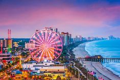 an aerial view of a ferris wheel on the beach with buildings and ocean in the background