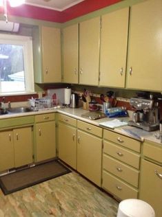 a kitchen with green cabinets and white appliances in the middle of the floor, next to a window that looks out onto a snowy field