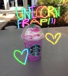 a starbucks drink sitting on top of a table next to neon signs that spell out the word unicorn frappi