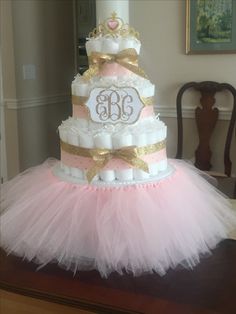 a three tiered cake decorated with pink and gold tutule, tiara and monogram on top