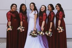 a group of women standing next to each other in front of a white wall holding bouquets