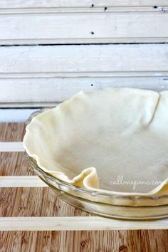 an uncooked pie crust in a glass dish on a wooden table with white stripes