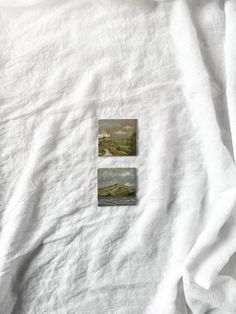 two paintings are placed on top of a white bed sheet that is partially covered with linen