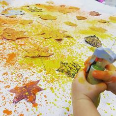 a child's hand is holding a paintbrush and painting leaves on a table