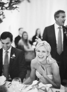 black and white photograph of bride laughing at groom's speech in wedding reception room