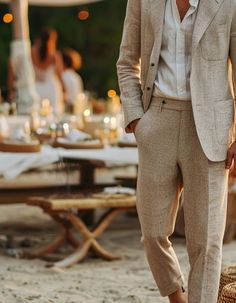 a man in a suit standing on the beach next to tables with candles and food