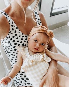 a woman holding a baby in her arms and wearing a polka dot dress with a bow