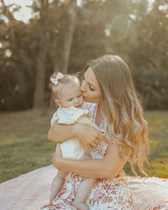 a woman holding a baby in her arms while sitting on a blanket with trees in the background