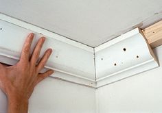 a hand that is reaching up to the corner of a wall with white paint on it