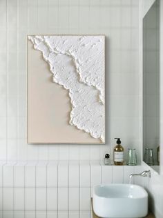 a bathroom with a sink, mirror and large painting on the wall in white tiles