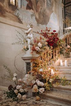 flowers and candles sit on the steps in front of a wall with an ornate painting