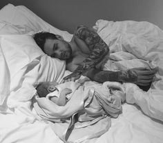 a man laying in bed with tattoos on his arm next to a baby wrapped in a blanket