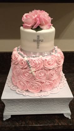 a cake decorated with pink roses on top of a white box and silver beaded cross