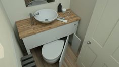 a white toilet sitting next to a wooden counter top under a bathroom mirror and sink