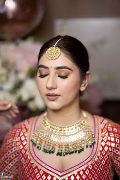 a woman in a red and gold outfit with jewelry on her head, looking at the camera