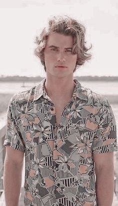 a man standing in front of a body of water wearing a shirt with an abstract pattern