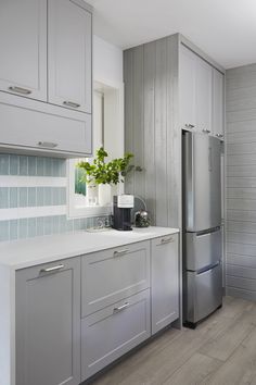 a kitchen with gray cabinets and white counter tops, along with a silver refrigerator freezer