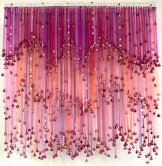 purple and pink streamers hanging from the ceiling in front of a white wall with red beads