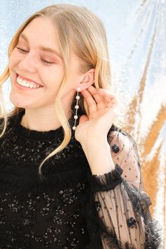 a woman with blonde hair is smiling and holding her earring up to the side