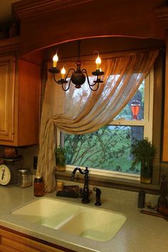 an image of a kitchen window with curtains on the windowsill and lights hanging over the sink