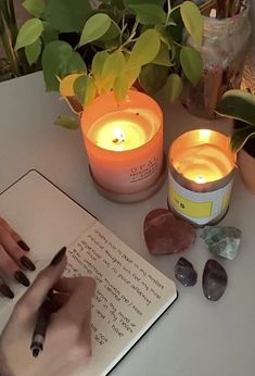 a person writing on a notebook next to candles and rocks