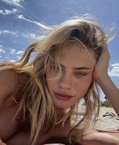 a young woman laying on top of a beach next to the ocean with her hair blowing in the wind