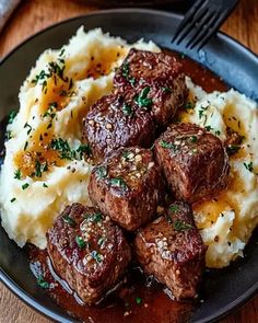 some meatballs and mashed potatoes on a black plate with a fork next to it