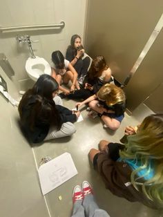 a group of women sitting on the floor in a bathroom next to a toilet paper