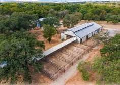 an aerial view of a horse barn in the middle of trees and dirt with a fence around it