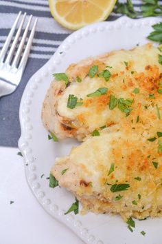 two pieces of chicken covered in cheese and parsley on a plate with a fork