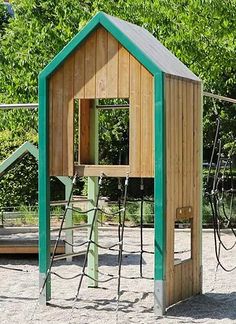 a wooden play structure in the middle of a park with swings and climbing ropes on it