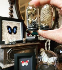 a person holding two small glass jars with butterflies inside them on top of a table