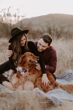 a man and woman sitting on a blanket with their dog