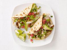 two tacos on a white plate with lime wedges