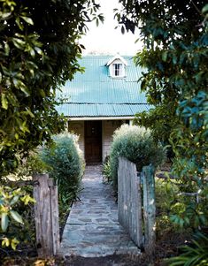 a small house with a green roof surrounded by trees and bushes on either side of the door