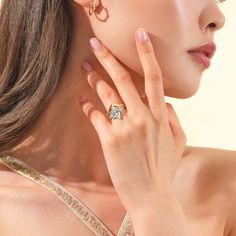 a woman with her hand on her ear wearing a diamond ring and gold dress shirt