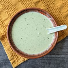 a bowl filled with green liquid sitting on top of a yellow napkin next to a spoon