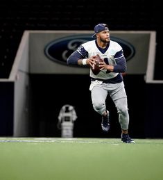 a man running with a football in his hand on the field at an indoor stadium