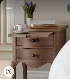 a wooden table with two drawers and a coffee cup on it next to a bed