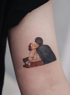 a woman's arm with a small tattoo of a man kissing a woman on the cheek