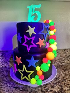 a birthday cake decorated with neon colored stars and beads on a granite countertop in front of a white wall