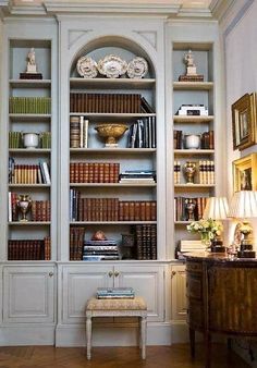 a room filled with lots of books on top of white bookcases next to a table