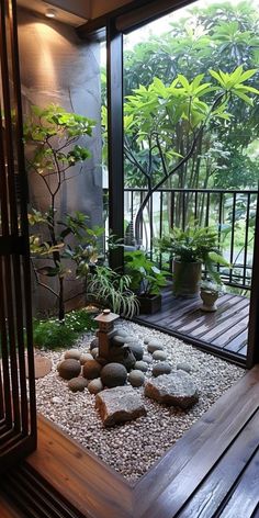 an indoor garden with rocks and plants on the ground, in front of a glass door