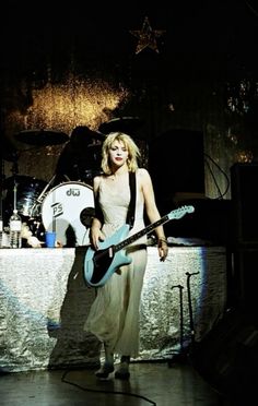 a woman standing in front of a table holding a guitar