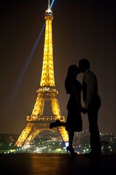 a man and woman standing in front of the eiffel tower at night with lights on