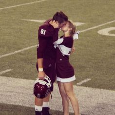 two people in uniform standing on a football field with their heads to each other and kissing