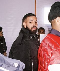 two men standing next to each other in front of a group of people wearing jackets