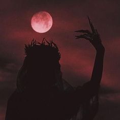 the silhouette of a person with their hands up in front of a red moon