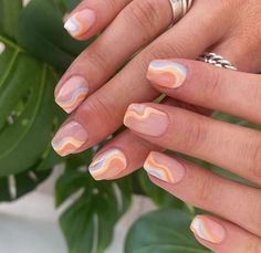 a woman's hand with pink, orange and white nail polish on it next to a plant